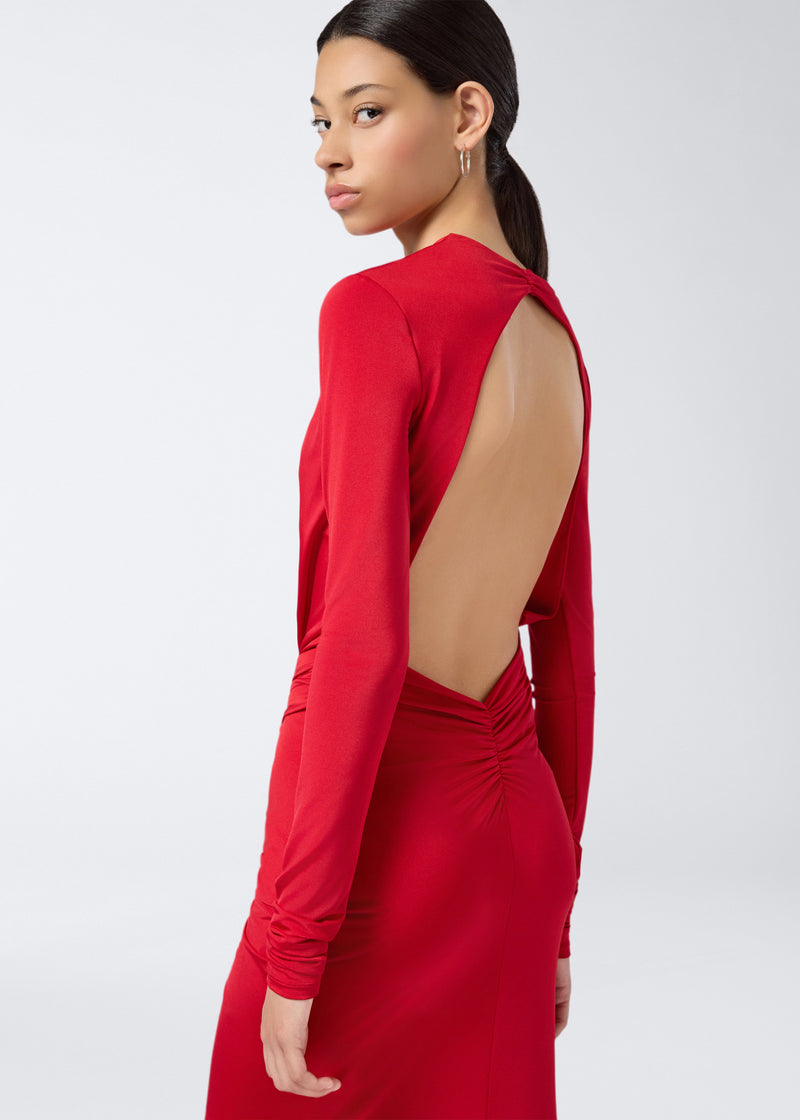 
                          Side view of a woman wearing the Zelda Maxi Dress, featuring a bold open back, ruched detailing, and long sleeves in vibrant red jersey fabric.
                        
