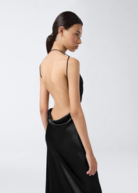 Side view of a model wearing the Vera Maxi Dress, showcasing its black shiny satin fabric, minimalist backless design, and thin adjustable straps.