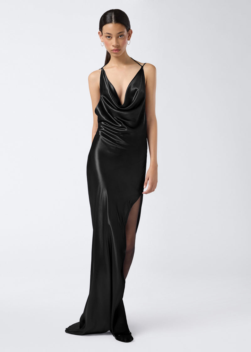
                          Frontal view of a model wearing the Vera Maxi Dress, a floor-length black shiny satin gown with a plunging cowl neck, adjustable straps, and side slit.
                        