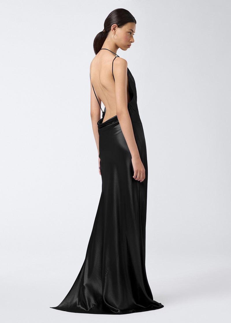 
                          Side view of a woman wearing the Vera Maxi Dress, a black shiny satin floor-length dress with a cowl neck, minimalist design, and strappy open back.
                        
