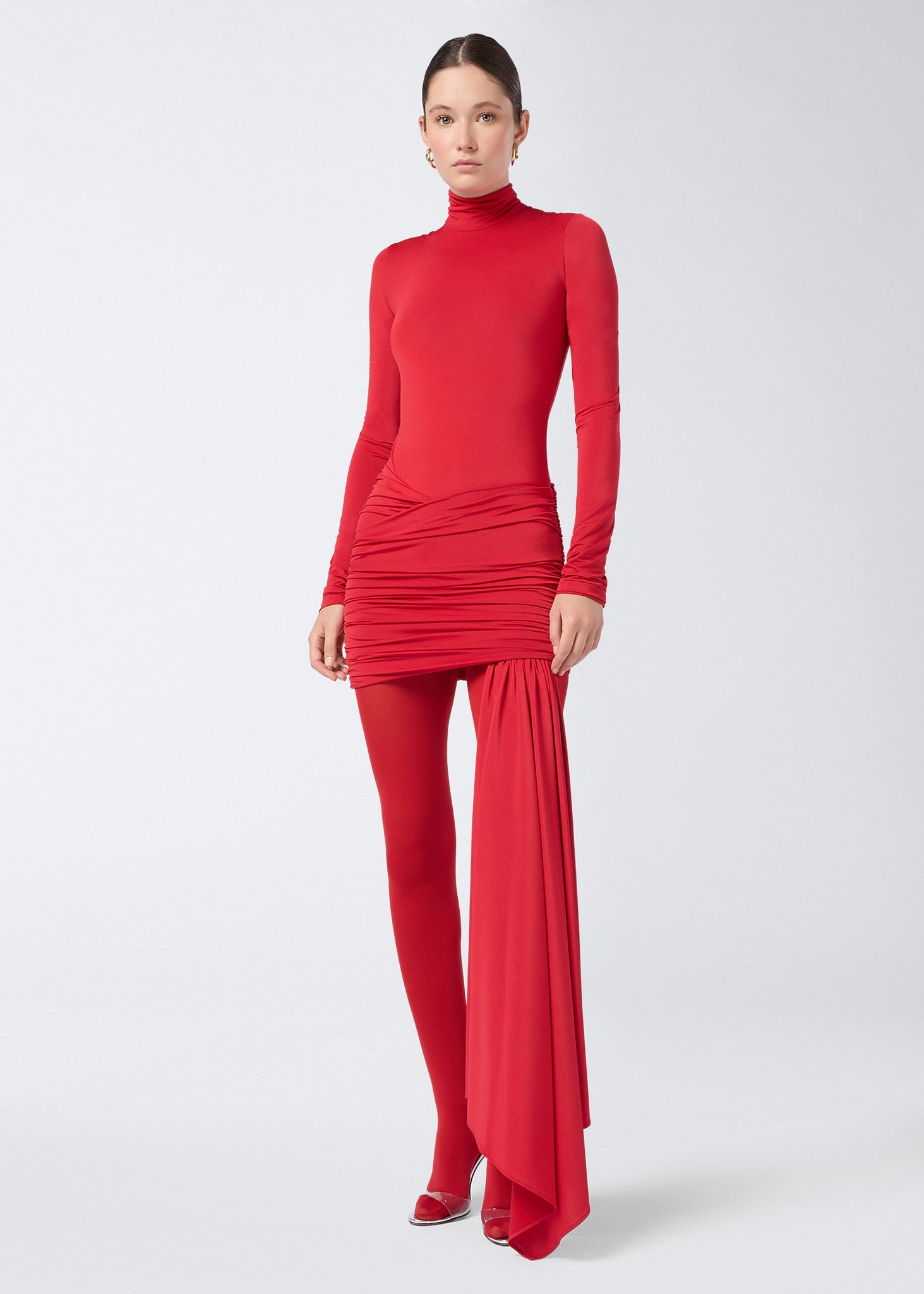 Frontal view of the Wendell Mini Skirt, a red lightweight jersey skirt with all-over ruching, a front cross-over accent, and a long panel suspended from the hem.