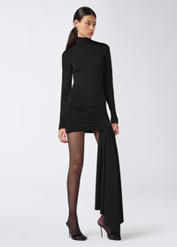 Frontal view of a woman wearing the Wendell Mini Skirt in black lightweight jersey, featuring all-over ruching, a cross-over front accent, and an asymmetrical long panel.