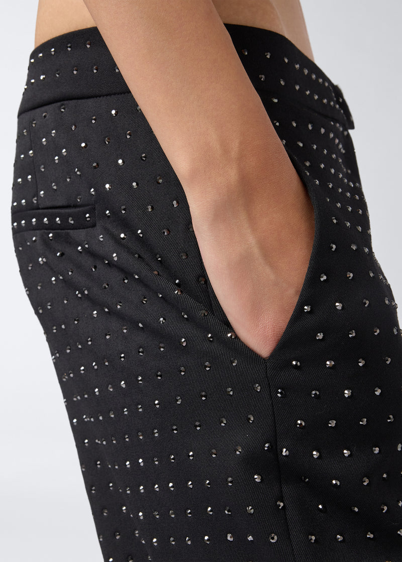 
                          Detail view showing the Gladys Pants in black wool and gabardine blend, featuring all-over small crystals and a hand in the pocket.
                        