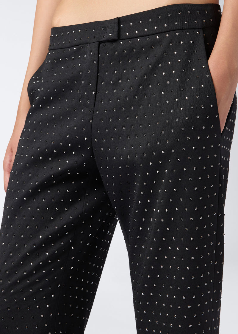 
                          Detail view of Gladys Pants showing black straight pants with all-over crystal embellishments, low waist, and front zip, button, and hook closure.
                        