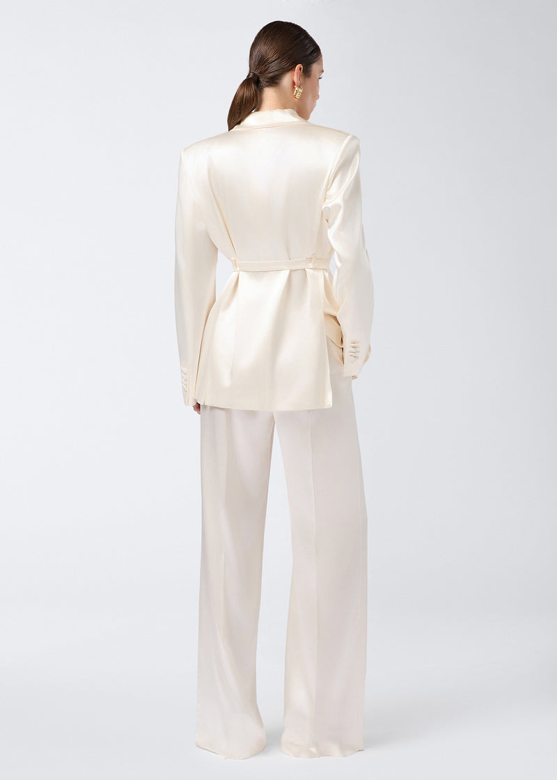
                          Rear view of model wearing Nathalie Pants in ivory shiny satin, featuring wide-hem design and high-rise waist, with matching satin blazer.
                        