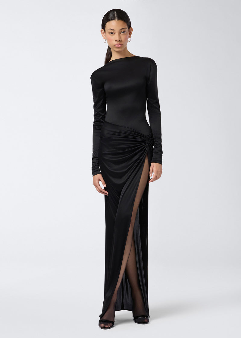 
                          Frontal view of a woman wearing the Sabrina Bodysuit in black shiny jersey, featuring long sleeves, a boat neckline, and styled with a high-slit skirt.
                        