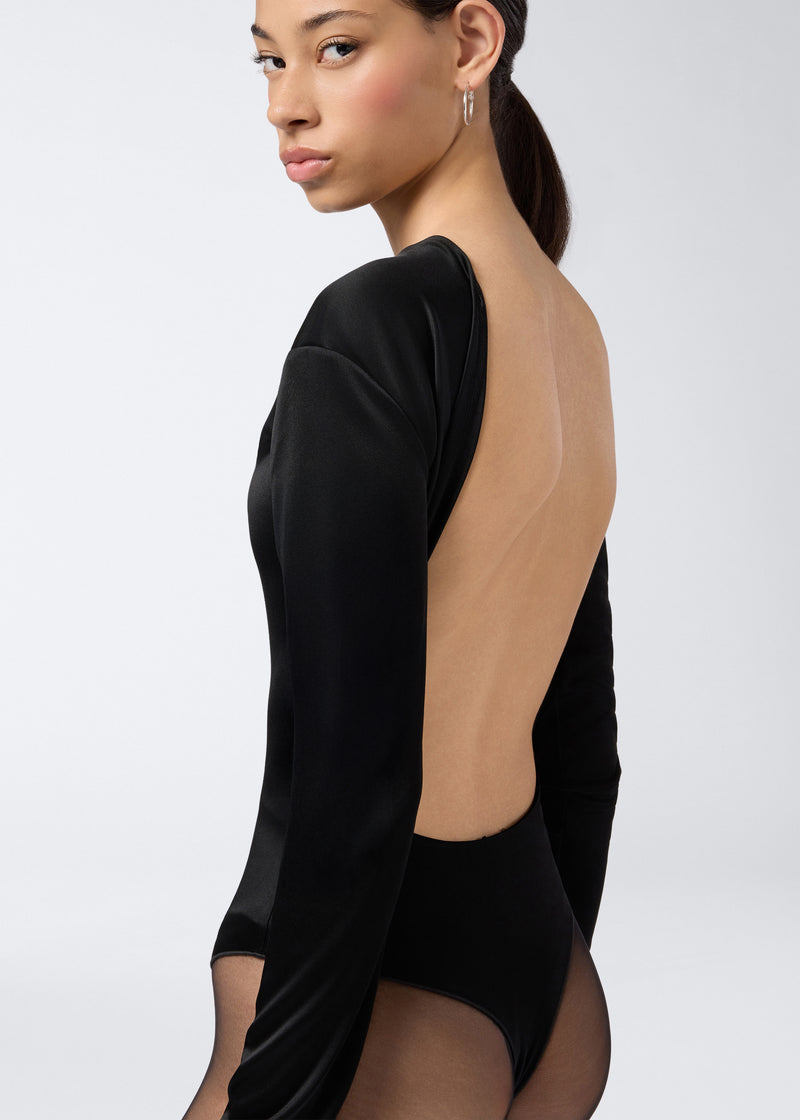 
                          Side view of a model wearing the Sabrina Bodysuit, showcasing its black shiny jersey fabric, long sleeves, and dramatic open back design.
                        