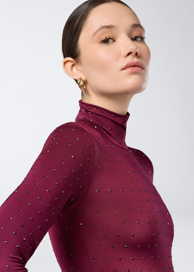 
                          Frontal view showing a woman wearing the Ziggy Bodysuit in cabernet jersey, long sleeves, turtleneck, and fully embellished with small crystals.
                        