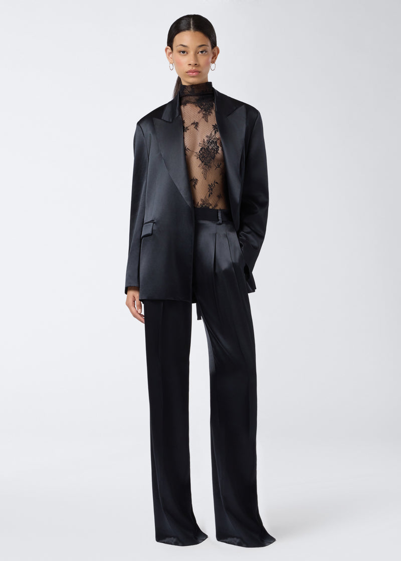 
                          Frontal view of a woman wearing the Ziggy Bodysuit, a sheer black lace bodysuit with long sleeves and a turtleneck, styled under a black suit.
                        