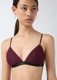 Frontal view showing a person wearing the New Guenda Bra in cabernet lace with black band underbust, black adjustable straps, and micro lace trim on the cups.