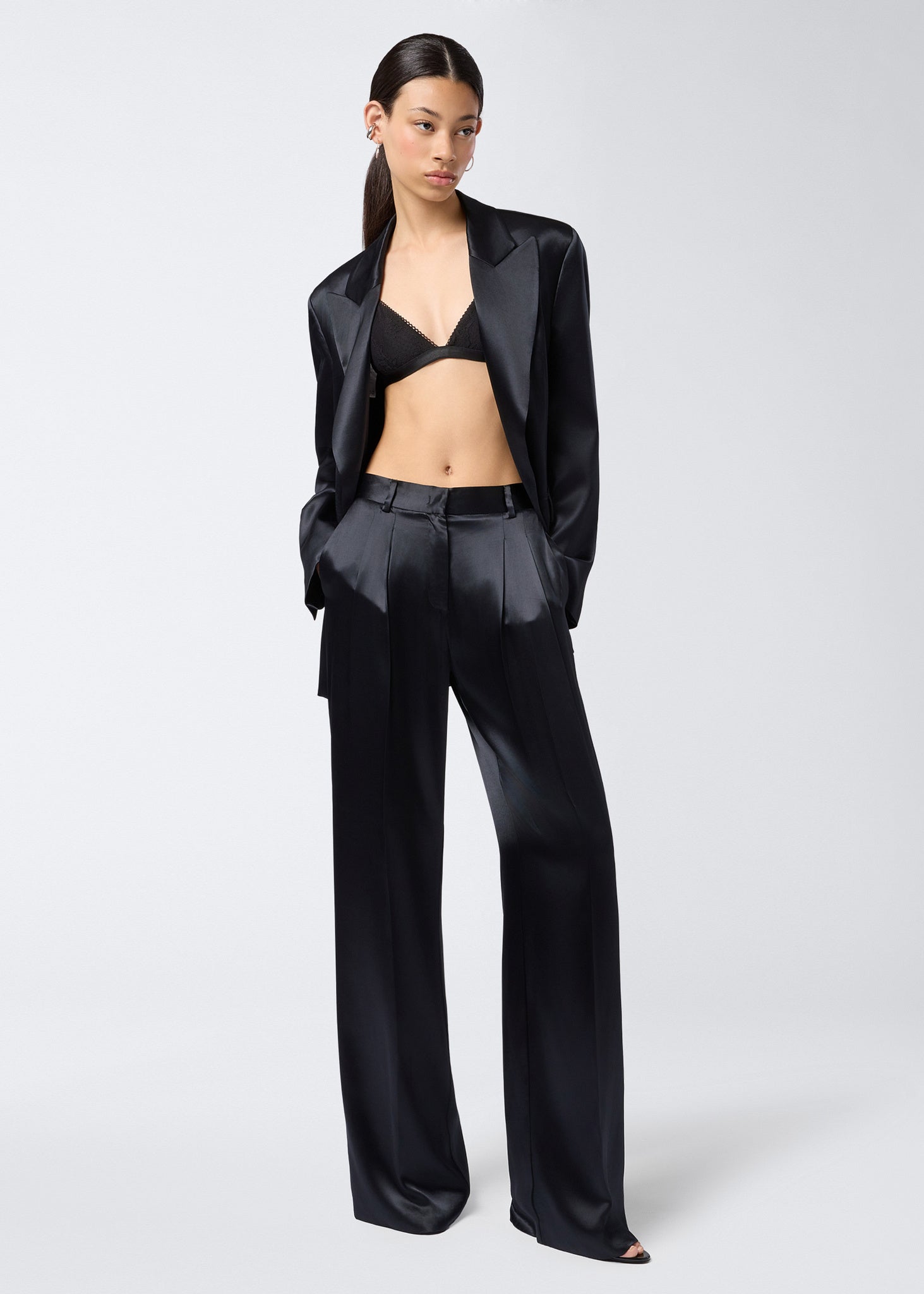 Frontal view of model wearing New Guenda Bra in black lace with micro lace trim, adjustable straps, and underbust band, styled with a black suit.