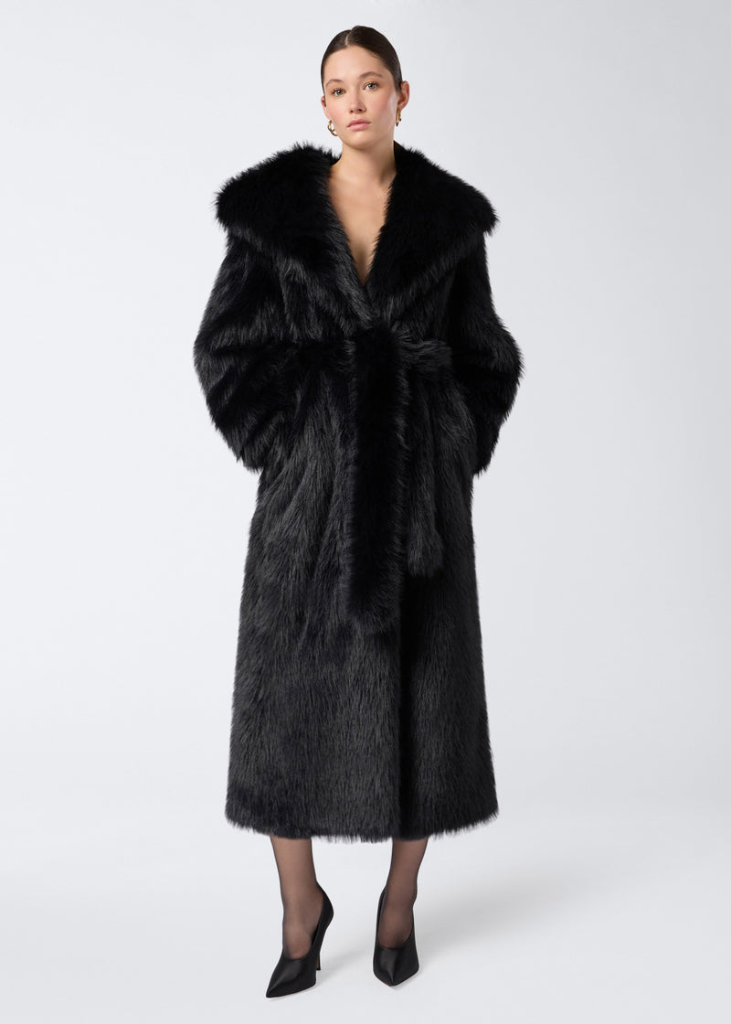 
                          Frontal view of a woman wearing the Winter Maxi Coat in black faux fur, featuring a large shawl lapel collar, matching belt, and long sleeves.
                        