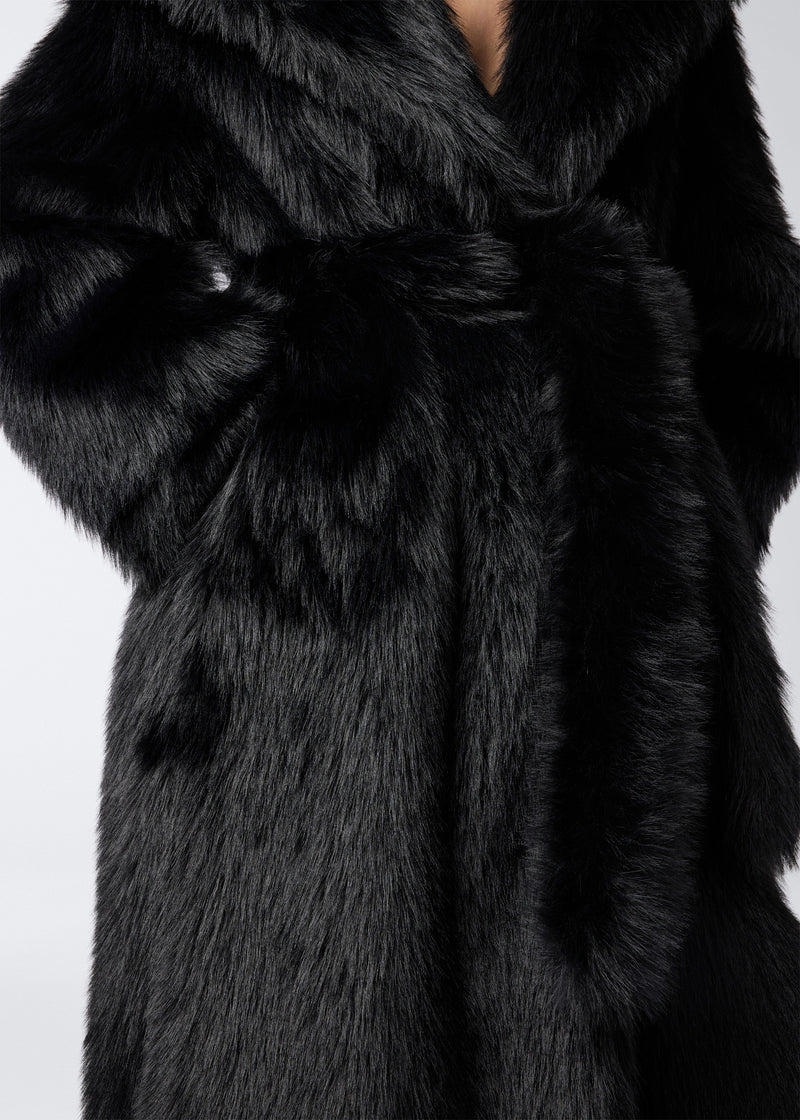 
                          Detail view of Winter Maxi Coat showing luxurious black faux fur texture, large shawl lapel collar, and matching waist belt on a woman&#39;s torso.
                        