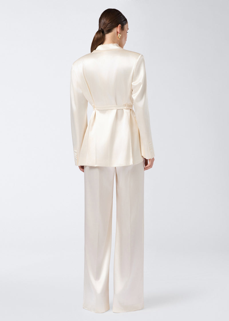 
                          Rear view of a woman wearing the Wilder Blazer in ivory shiny satin, featuring a belted waist, padded shoulders, and long sleeves with buttoned cuffs.
                        
