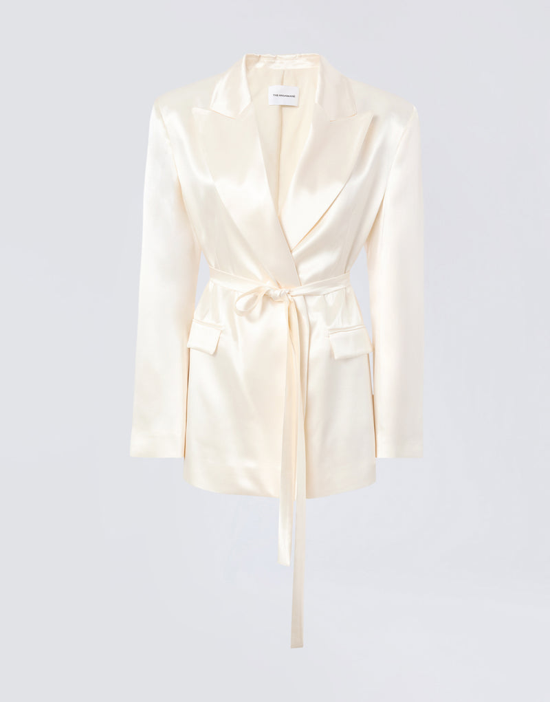 
                          Frontal view of Wilder Blazer in ivory shiny satin with peaked lapel, belted waist, padded shoulders, two flap pockets, and buttoned cuffs.
                        