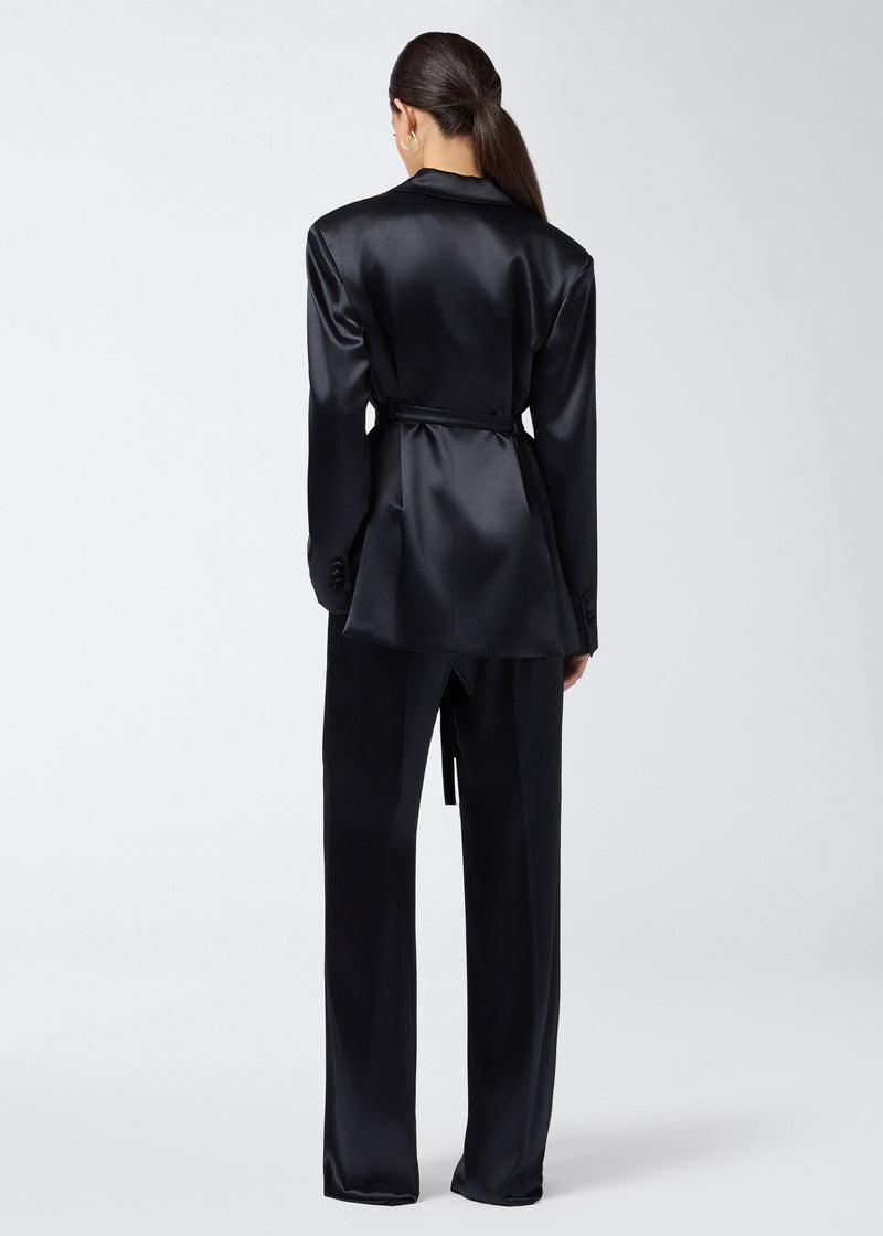 
                          Rear view of a woman wearing the Wilder Blazer in black shiny satin, featuring a waist belt, long sleeves, and tailored structure with padded shoulders.
                        