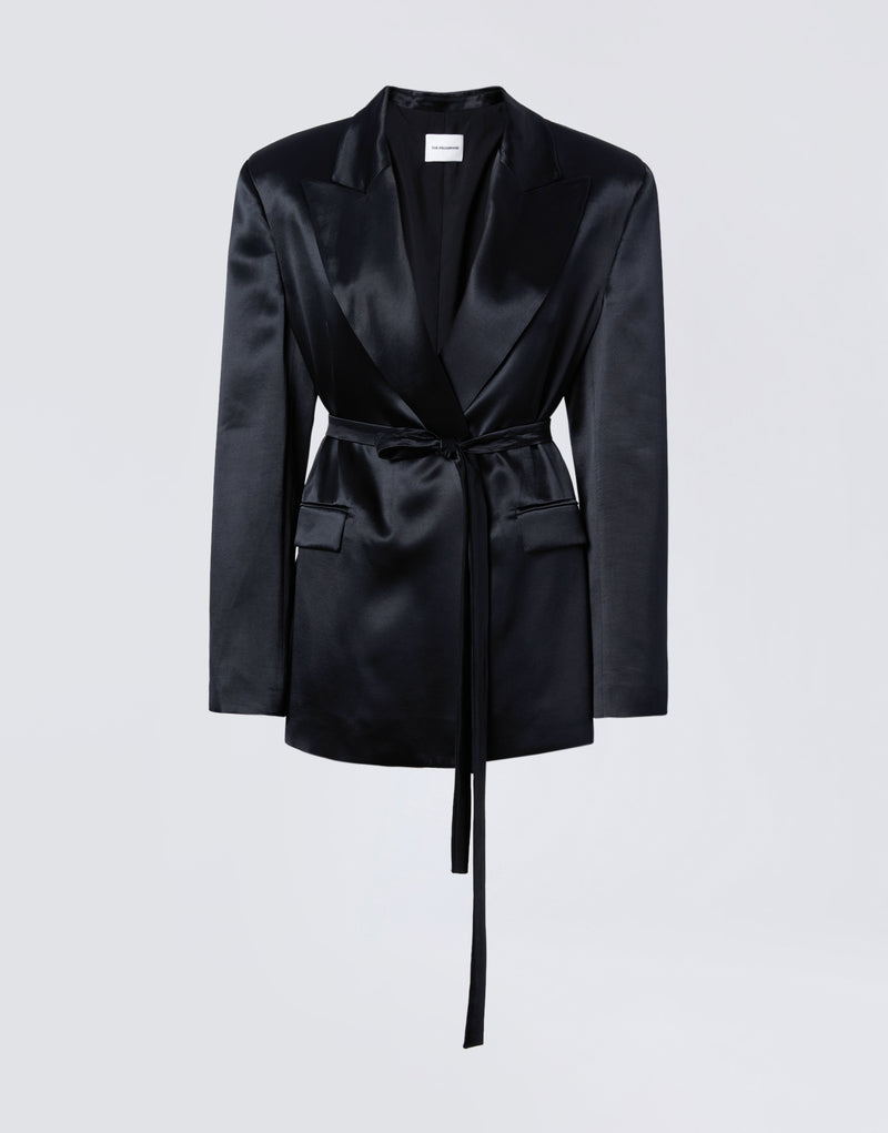
                          Frontal view of the Wilder Blazer, a black shiny satin women’s blazer with peaked lapel collar, padded shoulders, matching waist belt, two flap pockets, and long sleeves with buttoned cuffs.
                        