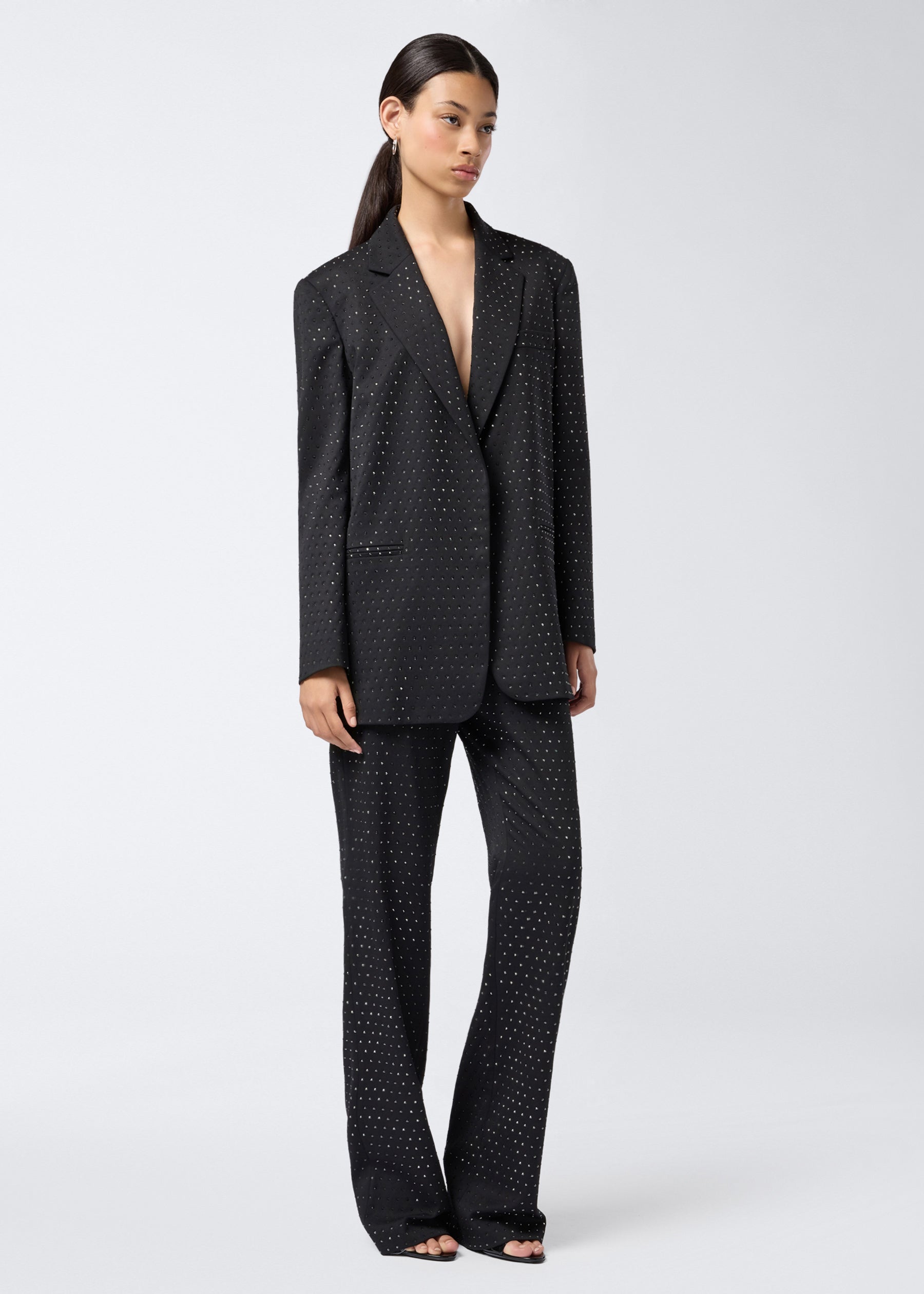 Frontal view of a woman wearing the Guia Blazer, an oversized black wool and gabardine blazer with crystal embellishments, notched lapel, and padded shoulders.