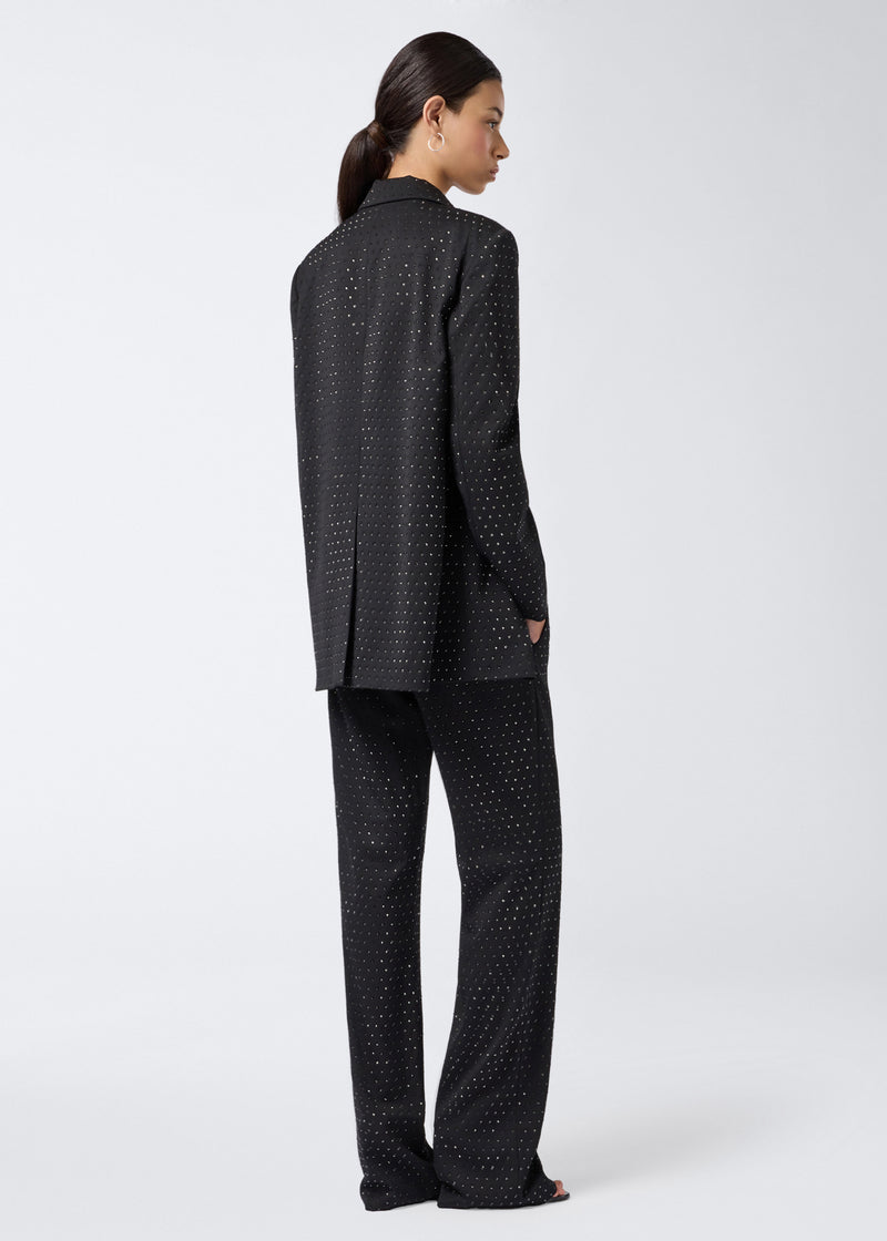 
                          Rear view of a woman wearing the Guia Blazer, a black crystal-embellished oversized blazer with subtle pattern, paired with matching black trousers.
                        