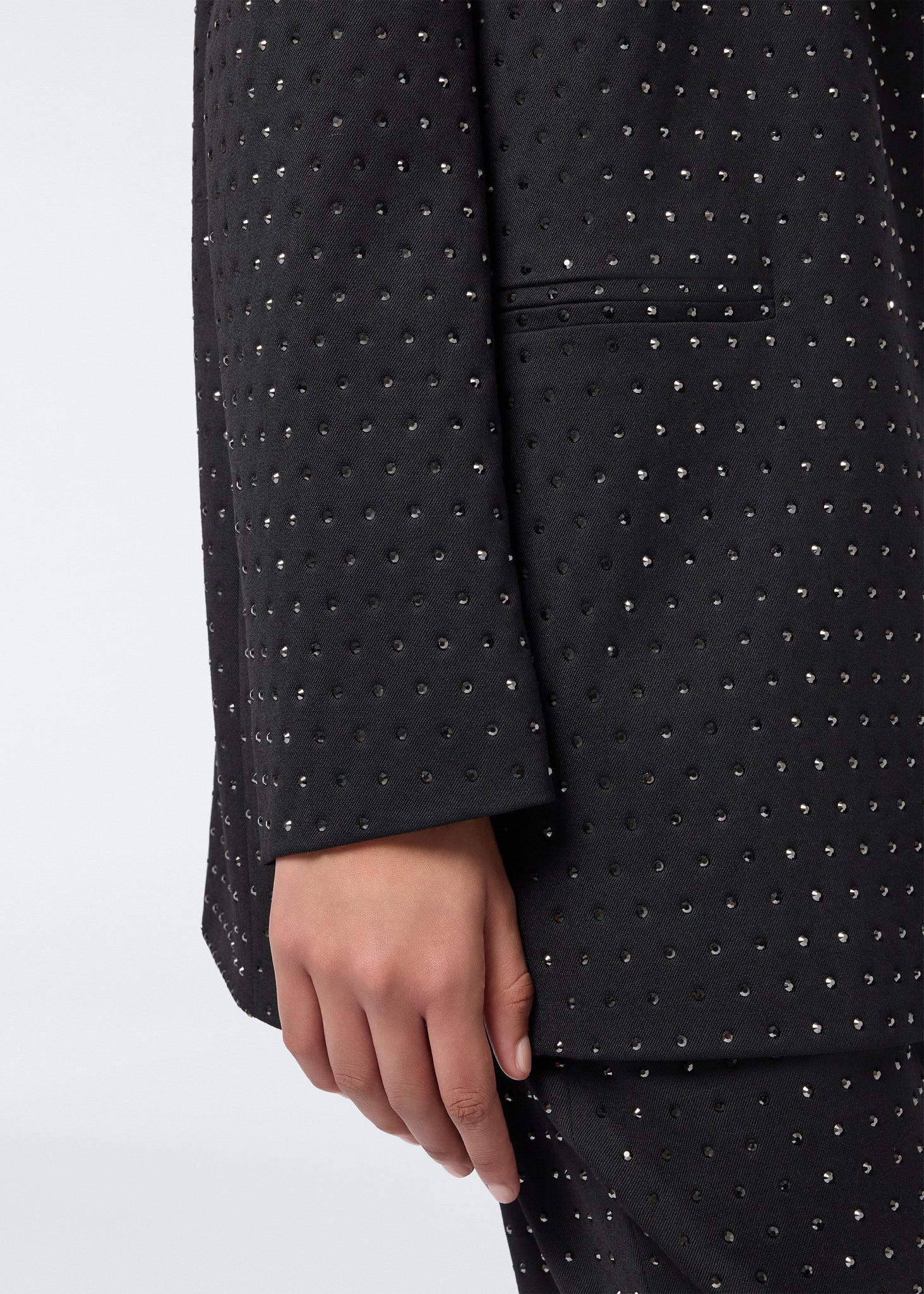 Detail view of the Guia Blazer showing a close-up of the black wool and gabardine fabric embellished with small crystals, featuring a jetted pocket and sleeve.