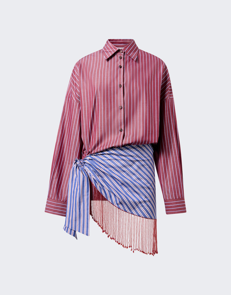Frontal view — Jolene Mini Dress: rouge noir striped shirt buttoned and tucked at the waist, blue-striped panel tied into an asymmetric skirt draping with red fringe, studio background.