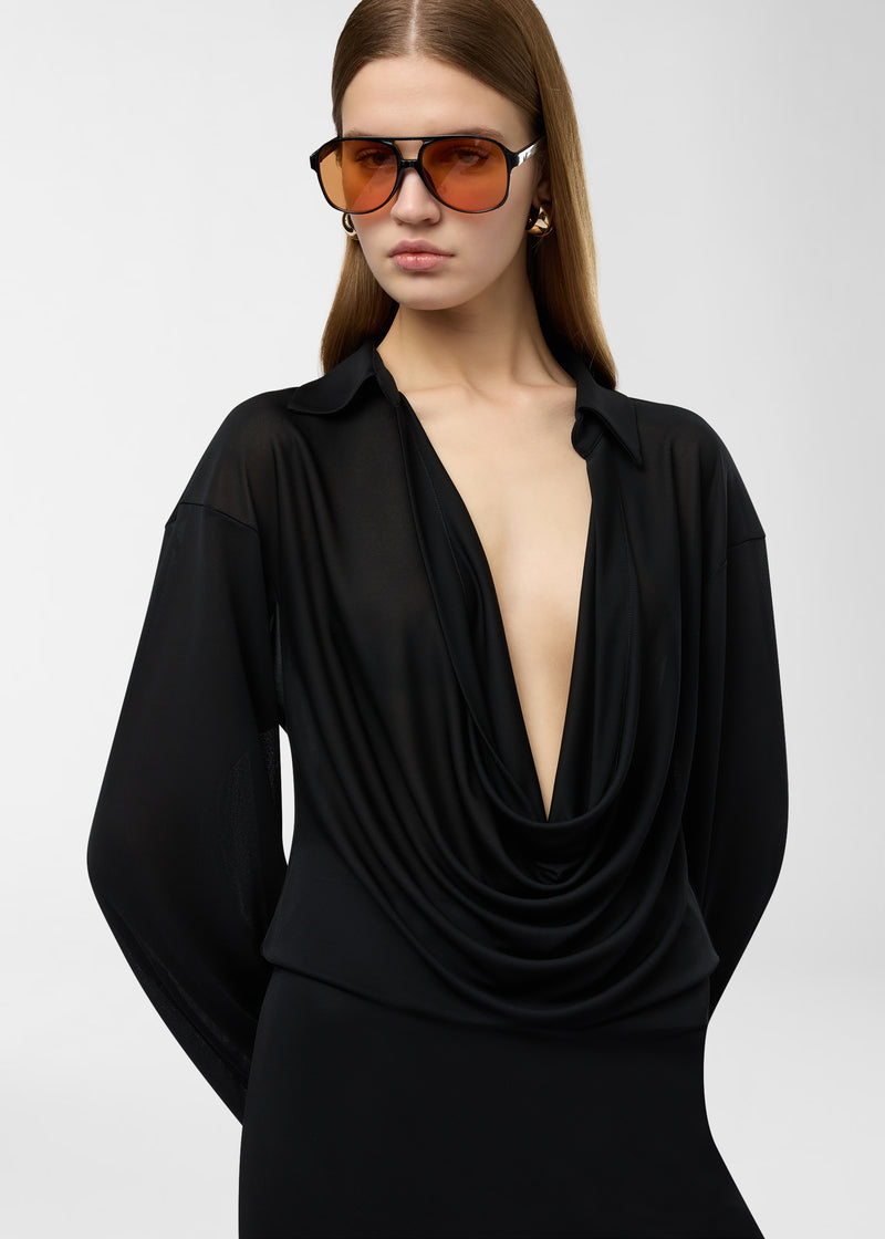 Frontal view: Model wearing Lilia Midi Dress, draping black jersey-chiffon with deep plunging V-neck and spread collar, long exaggerated single-button cuffs and fluid, slightly sheer silhouette.