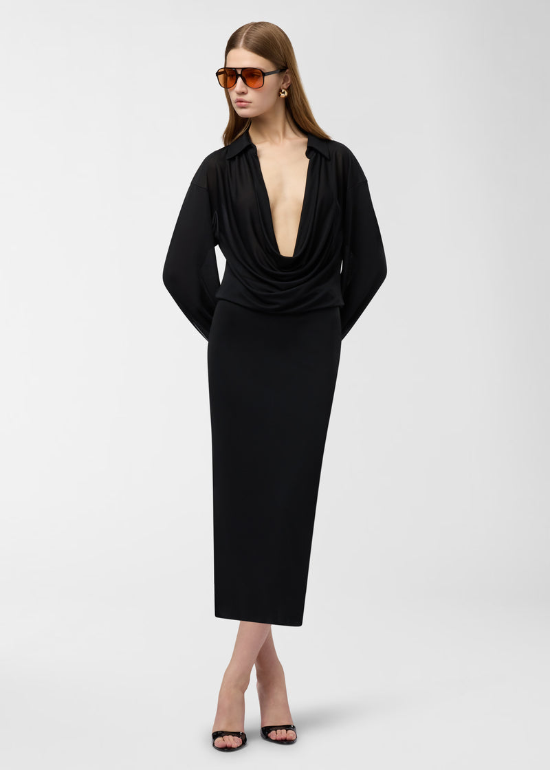 Frontal view: Model wearing Lilia Midi Dress stands with hands behind her back against a studio background, showcasing deep draped V-neck and slim midi skirt.
