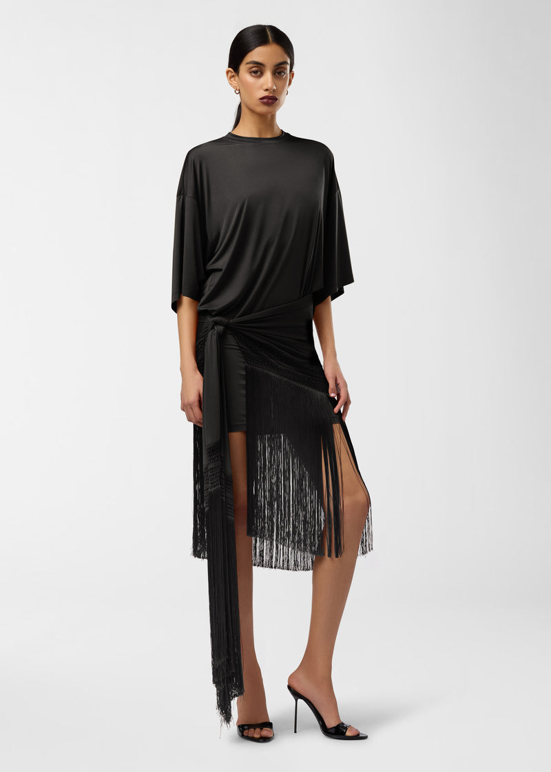 Frontal view: Model wearing Azul Midi Dress — black jersey T-shirt dress with crew neck, butterfly sleeves, side-gathered knot and long fringe-trimmed asymmetric hem.