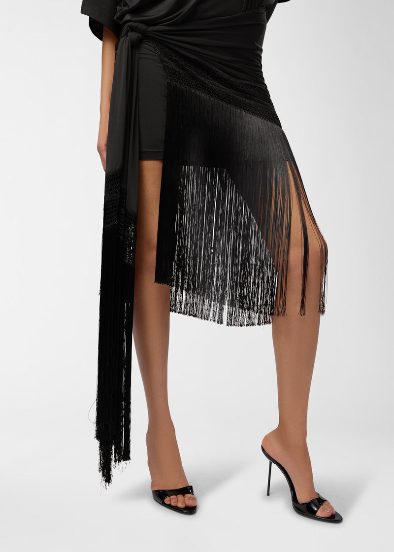 Frontal view — Azul Midi Dress: model's lower torso and legs wearing black, side-gathered midi dress with long fringe-trimmed asymmetric hem cascading over stiletto mules.