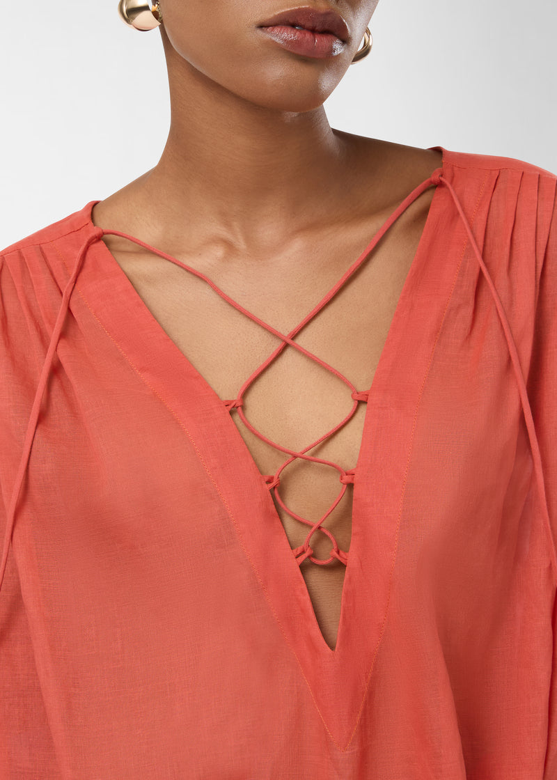 Detail view — Indira Mini Dress showing tangerine cotton muslin with stitched shoulder pleats, lace-up ties crisscrossing over a plunging V neckline, worn on model chest-up.