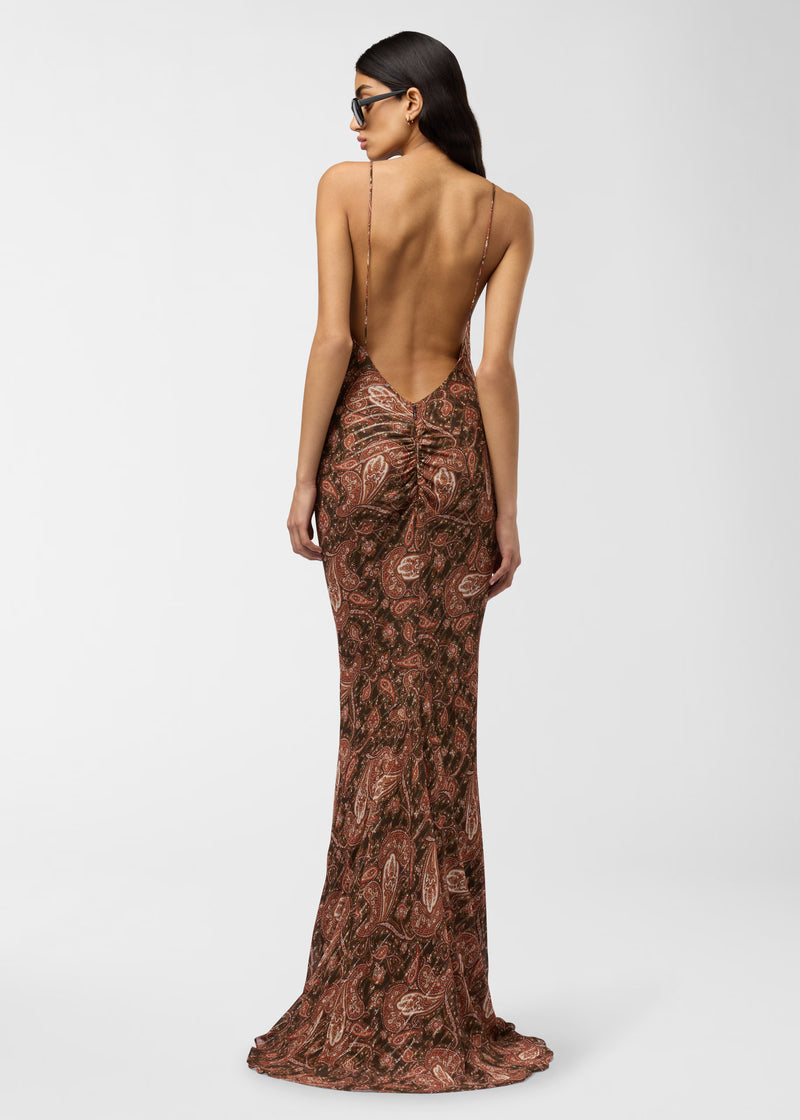 Rear view — Model wearing Ninfea Maxi Dress stands facing away, showing deep scoop back, thin spaghetti straps, ruched waist, and long paisley mermaid skirt on white background.