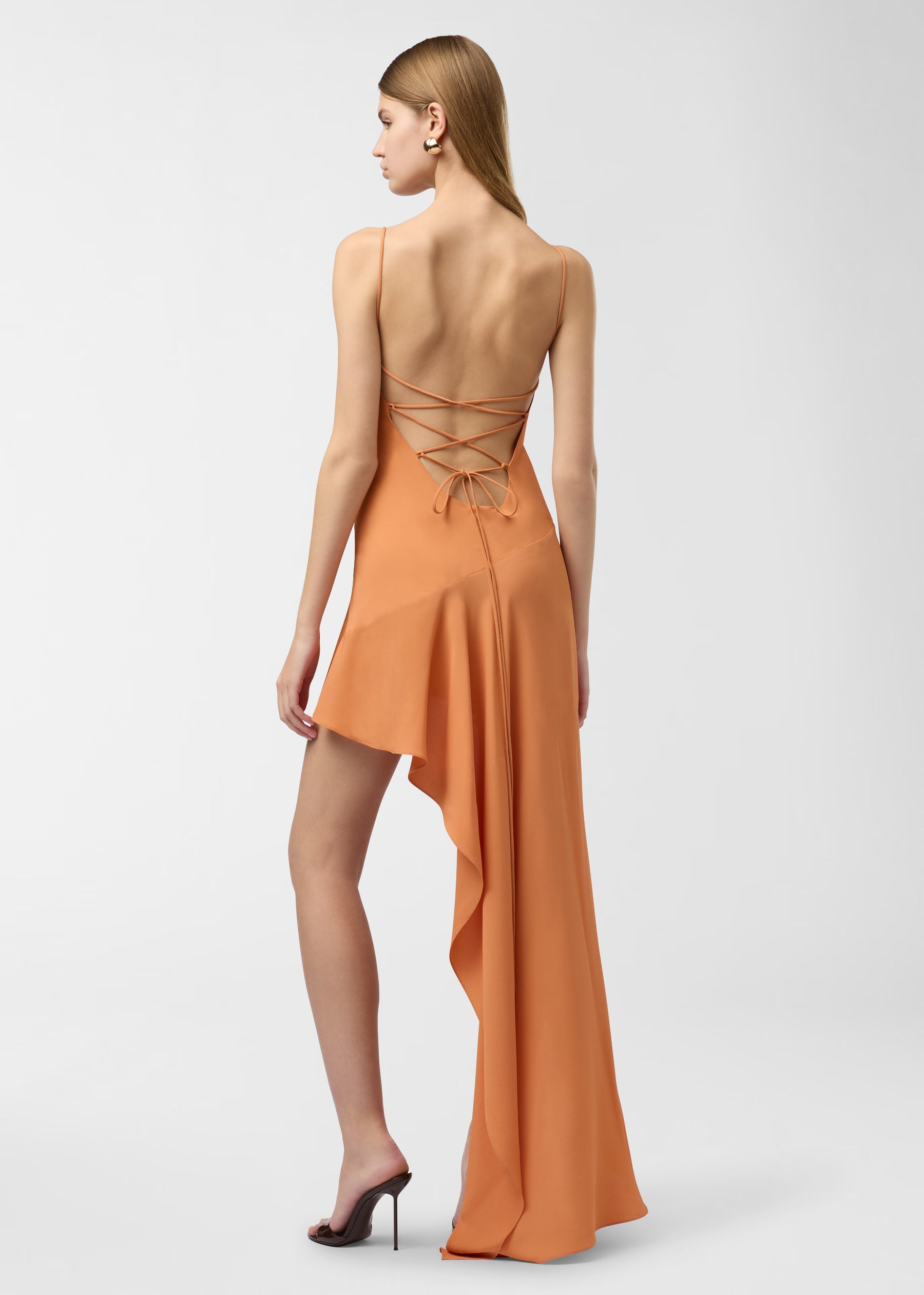 Rear view: Lauren Maxi Dress worn by model, showing spaghetti straps and lace-up back, undulating asymmetrical skirt cascading into a long train against a plain studio background.