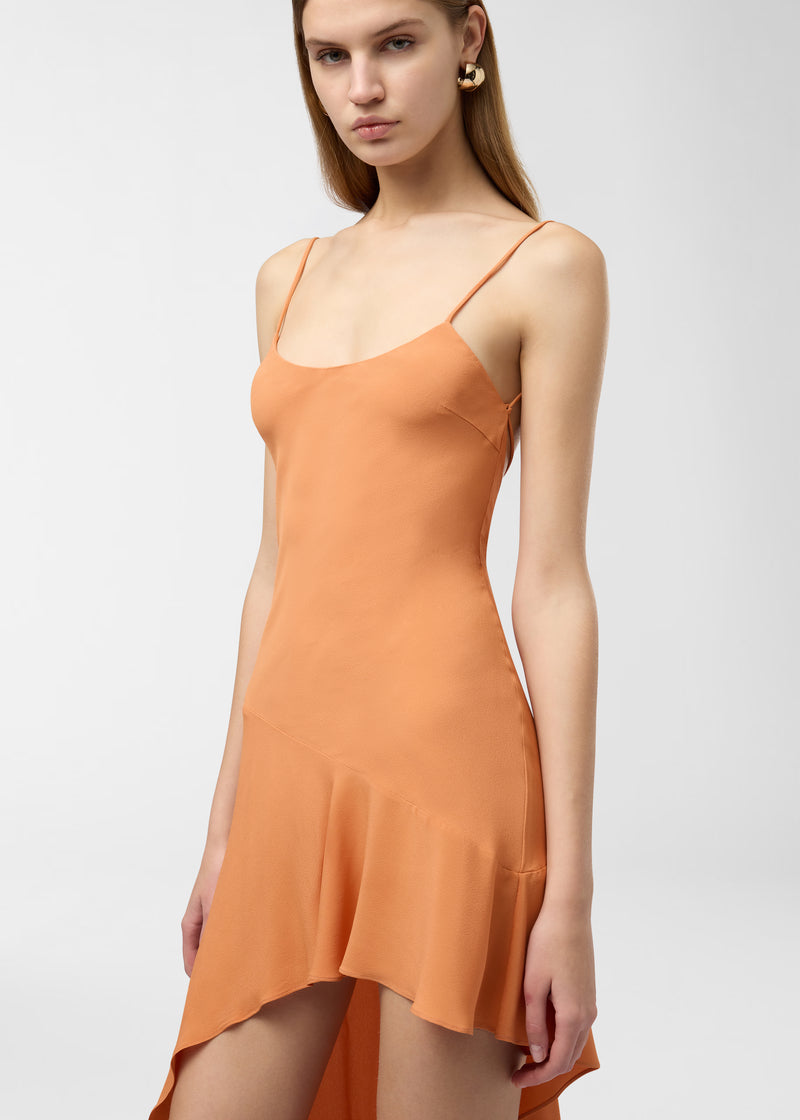 Frontal view, Lauren Maxi Dress worn by model, draping in tangerine crepe de chine with curved neckline, spaghetti straps and asymmetrical undulating hem, studio white background.