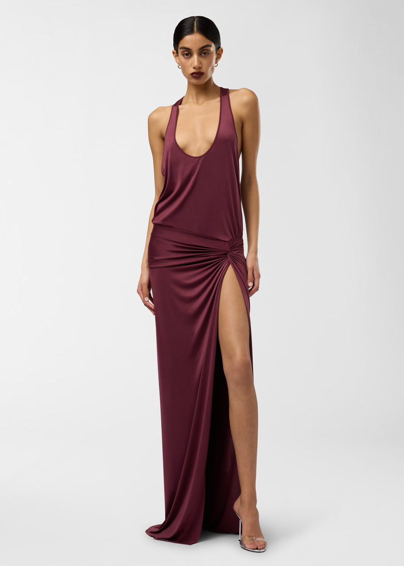 Frontal view: Juno Maxi Dress on a model standing straight, showcasing a plunging scoop neck and racerback, ruched knot at the hip and a high thigh slit in rouge noir.