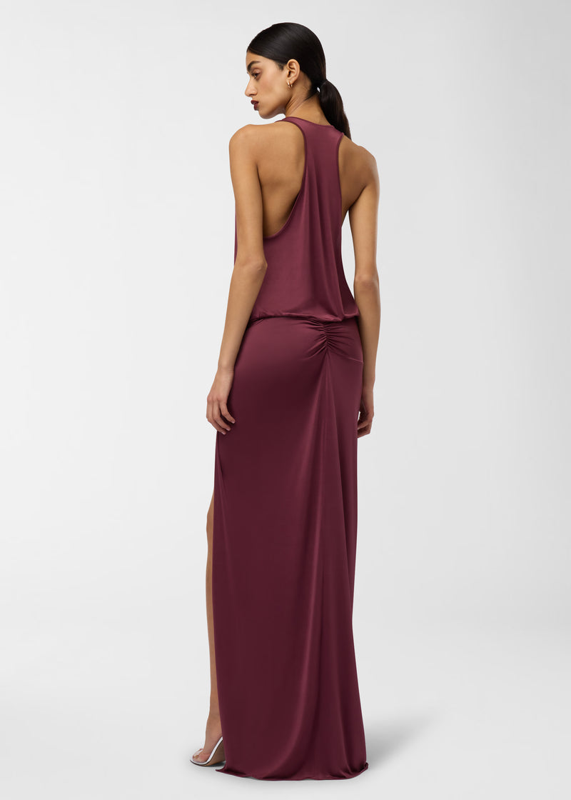 Rear view — Juno Maxi Dress worn by model, showing racerback bodice, plunging scoop, gathered knot at hip with ruched back, high side leg slit, rouge noir lightweight jersey.