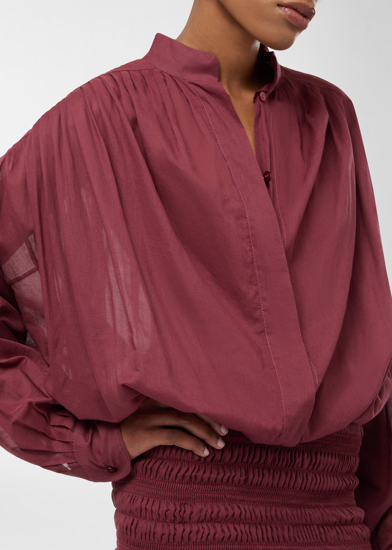 Frontal view — Rania Mini Dress: model in loose shirt-style bodice in rouge noir with pleated shoulders, mandarin collar, button placket and smocked frilled skirt.