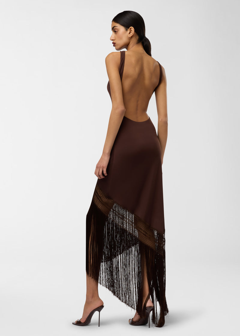 Rear view: Marisol Maxi Dress worn by a model — dark brown tank-style maxi with a deep open back, fitted racer-style bodice, asymmetrical skirt featuring openwork band and long fringed hem.