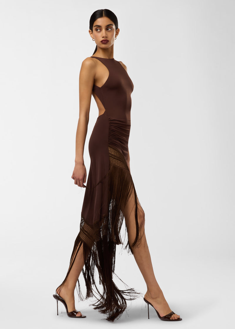 Side view: Model wearing Marisol Maxi Dress shows racer-style bodice and open back, ruched hip, openwork skirt panels, and long fringed hem drifting while walking.