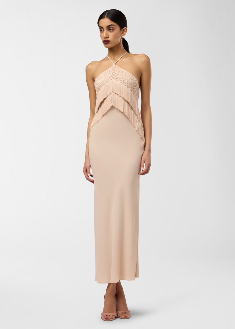 Frontal view: Model wearing Reina Midi Dress stands facing forward in a plain studio, showcasing its bandeau halter top with layered fringe and long peach midi skirt.