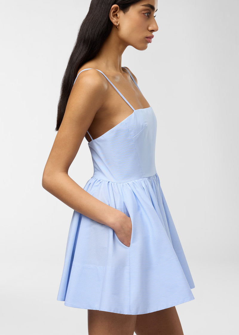 Side view — Carrie Mini Dress worn by a model, showing straight-across neckline, thin straps, fitted bodice and gathered high-rise micro-striped skirt with hand-in-pocket.