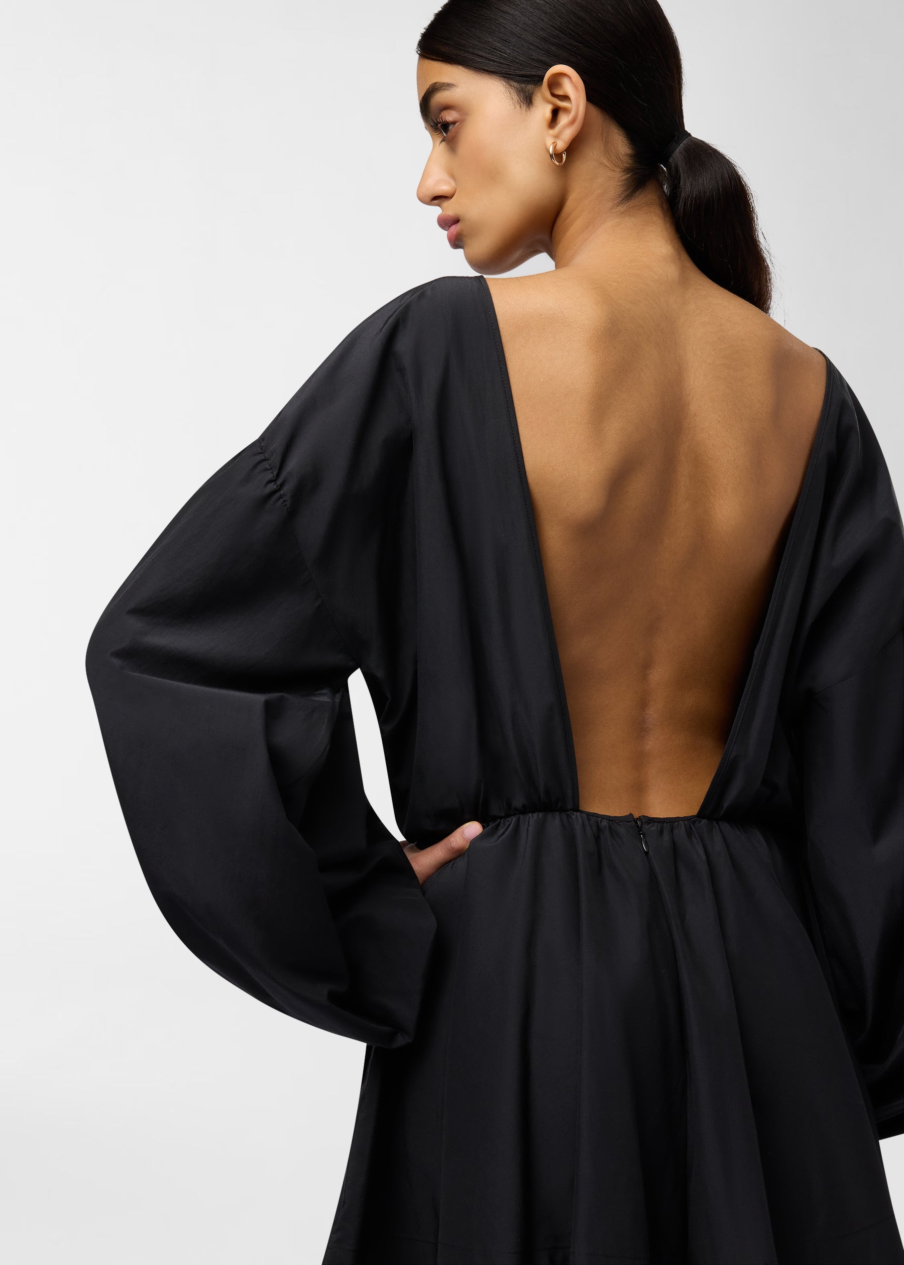 Rear view — Clara Playsuit: Model in black shows deep open back, voluminous balloon sleeves, cinched waist and A-line skirt, posed against a plain white background.