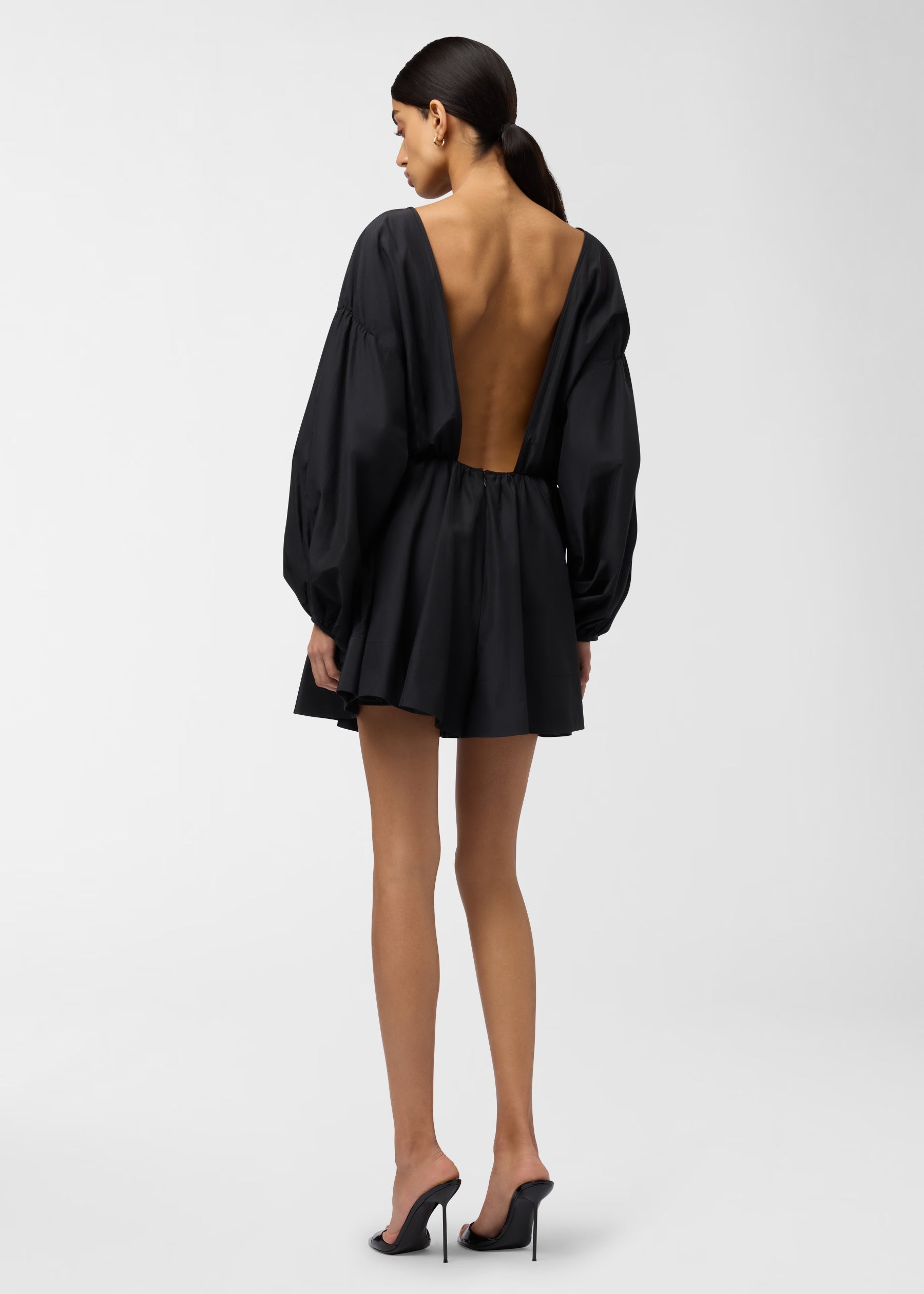 Rear view — Model in Clara Playsuit faces away, showing deep open back, balloon sleeves, cinched waist and short A-line skirt on a plain studio background.