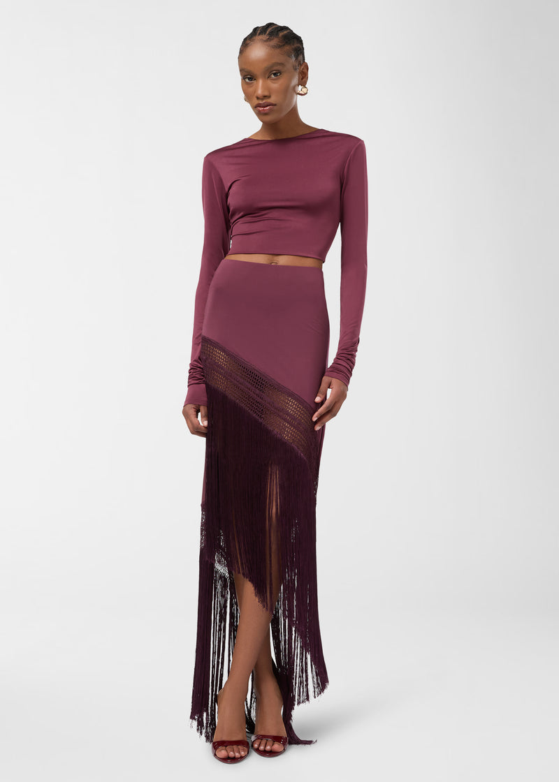 Frontal view — Model wearing Marisol Skirt standing, showing high-rise waist, asymmetrical hem with openwork weave and long straight fringe in rouge noir jersey.