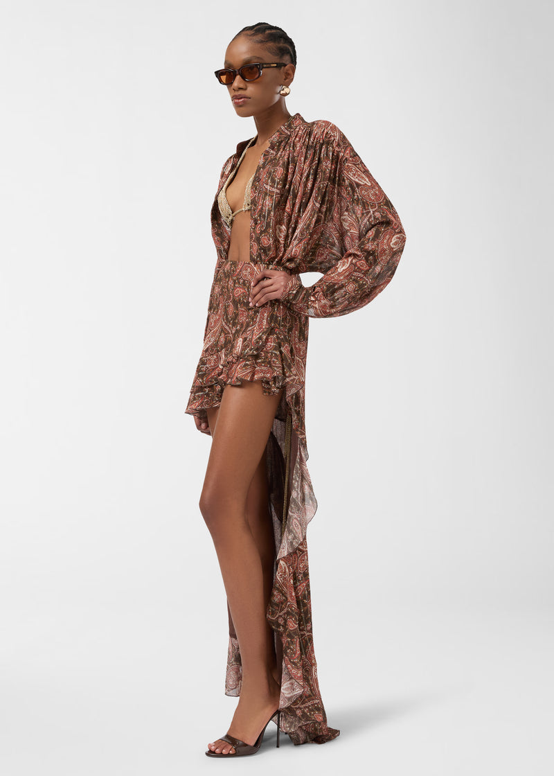 Side view — Model wearing Camelia Maxi Skirt, standing with hand on hip, showing high-rise paisley georgette, asymmetrical ruffled cascade draping to the floor.