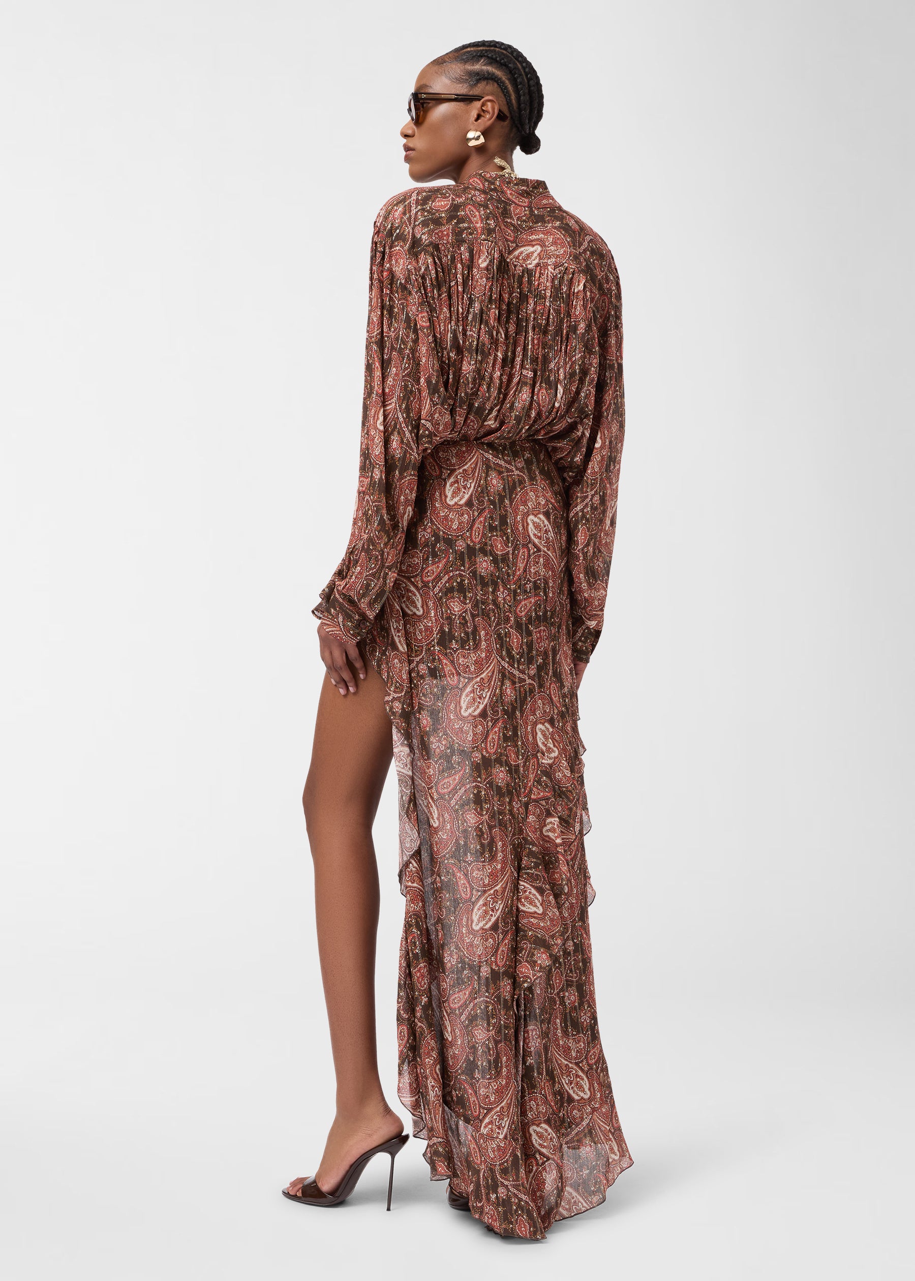 Rear view: Model wearing Camelia Maxi Skirt drapes asymmetrically from high-rise waist, paisley georgette flowing to floor with ruffled tiers against plain white backdrop.