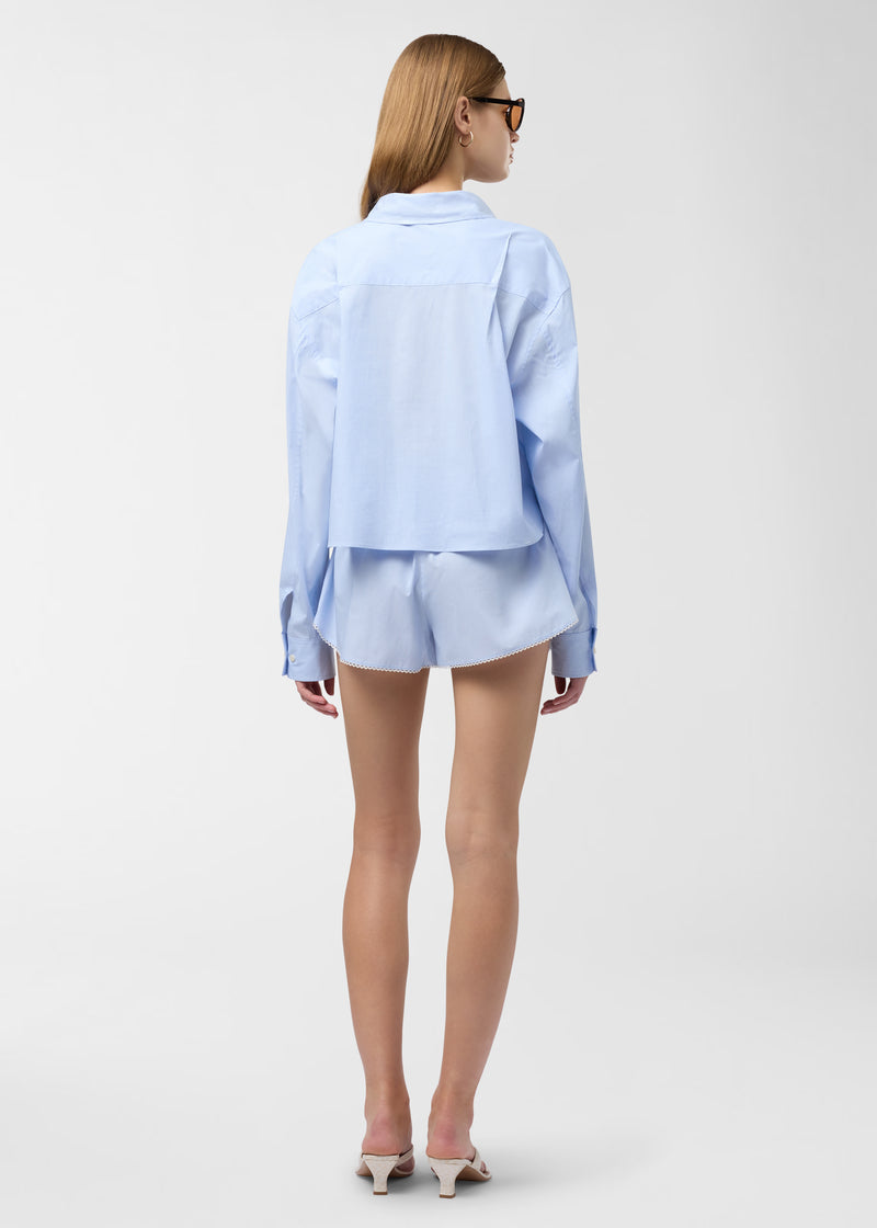 Rear view — Model wearing Arabella Shorts standing against neutral background, showing light-blue and white micro-striped boxer shorts with micro lace trim, low-rise elastic waistband and side slit pockets.