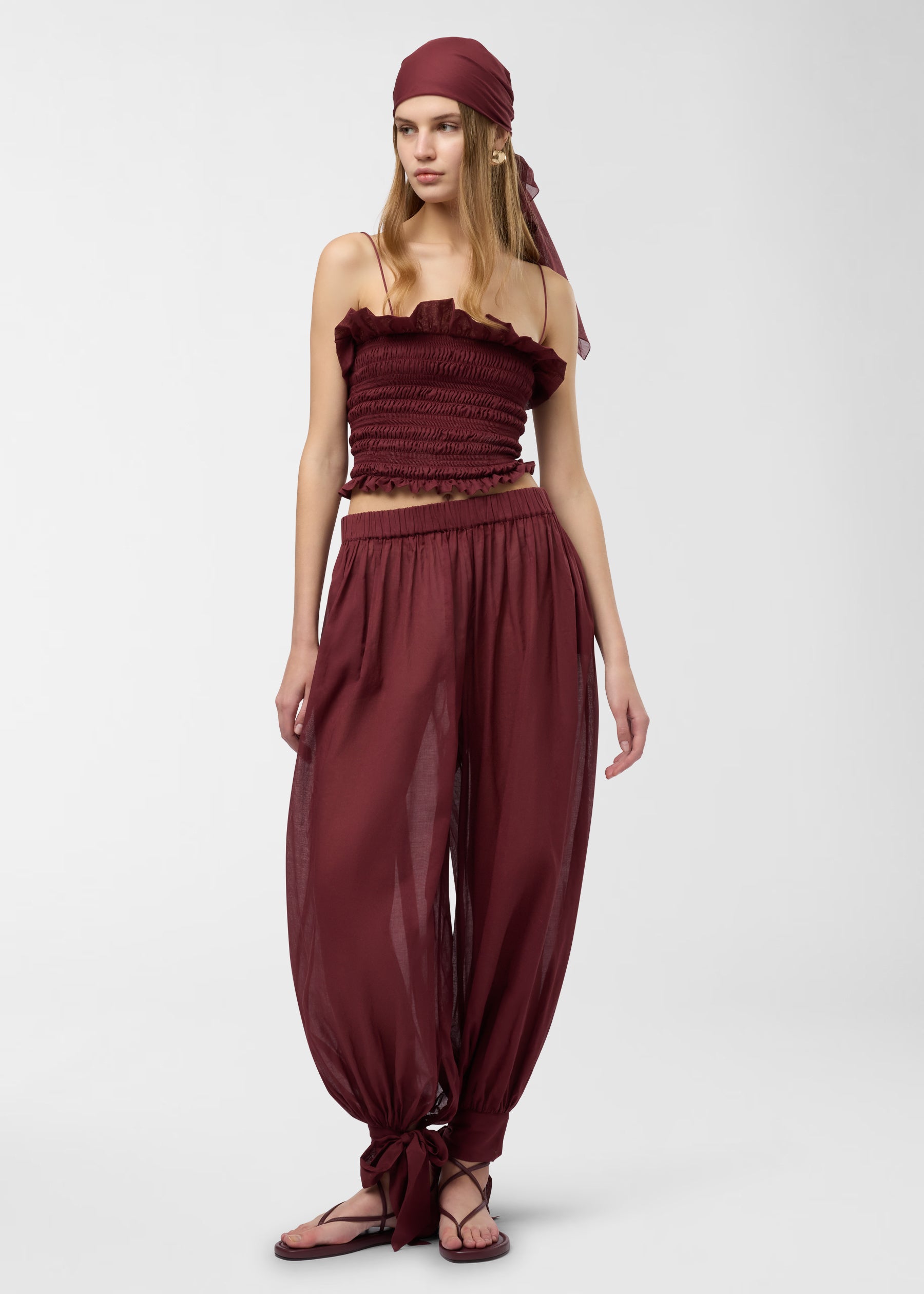 Frontal view — Model wearing Noor Maxi Pants stands facing forward, showing semi-sheer rouge noir cotton muslin, wide balloon legs tapering to tied bows at the ankles.