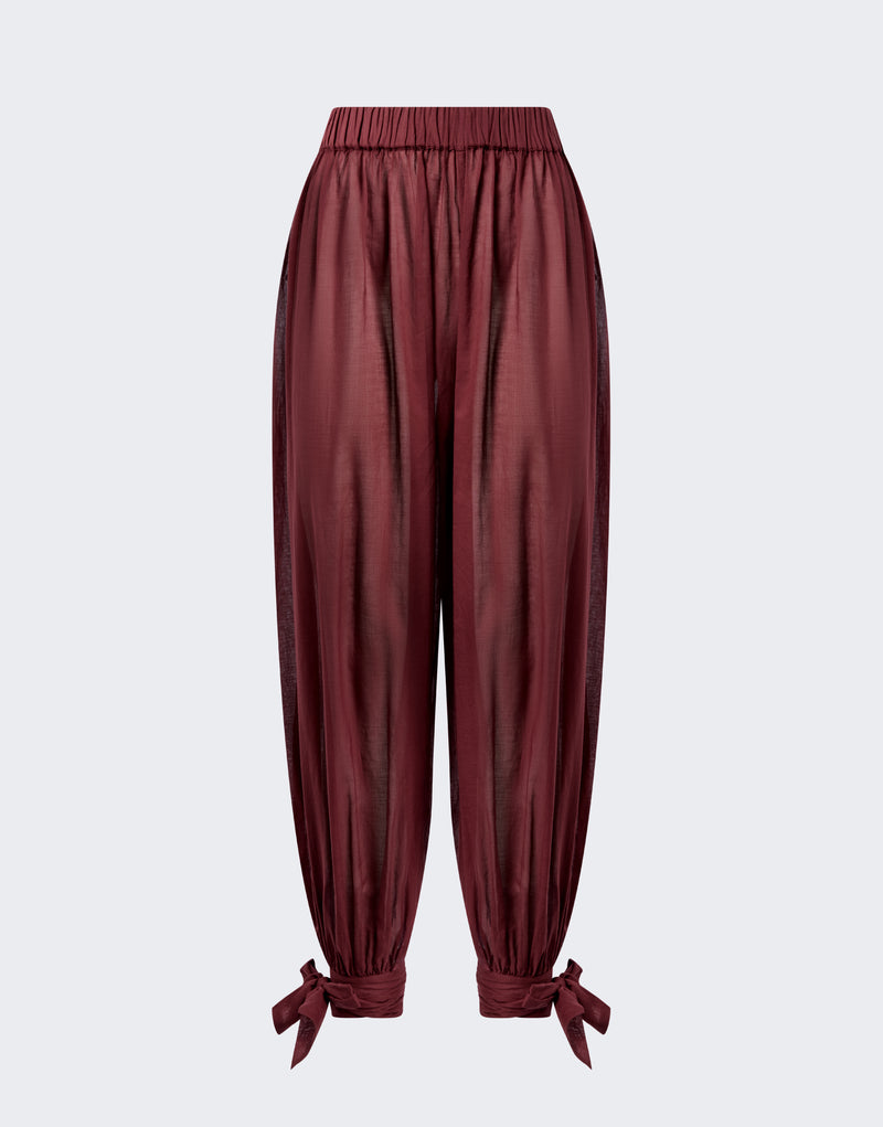 Frontal view — Noor Maxi Pants hang flat against a neutral background, showing rouge noir semi-sheer cotton muslin, elastic low-rise waistband, wide balloon legs tapering to tied ankle bows.
