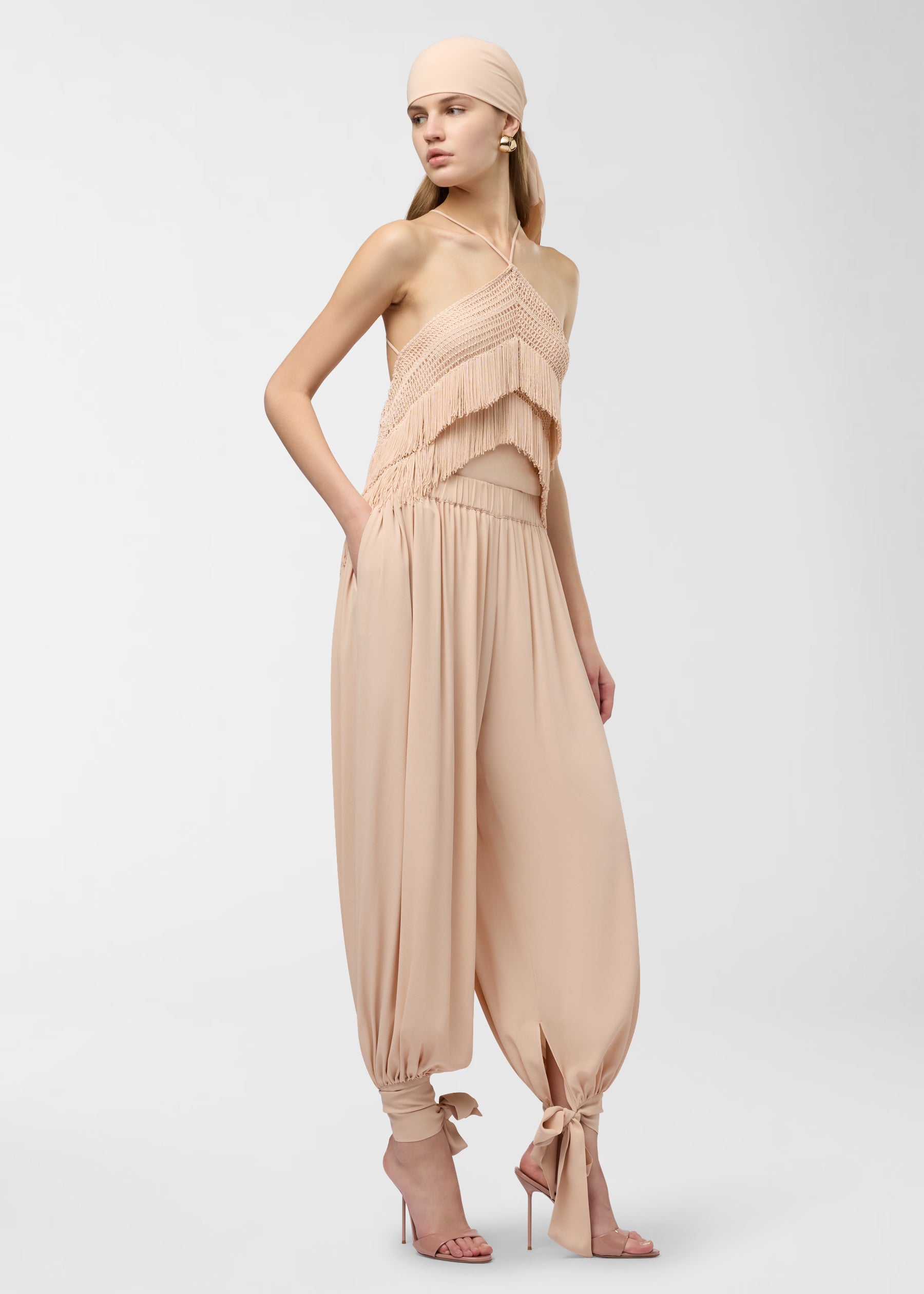 Side view — Noor Maxi Pants worn by model with hand in pocket; peach crepe de chine balloon silhouette tapered and tied at ankles against light background.