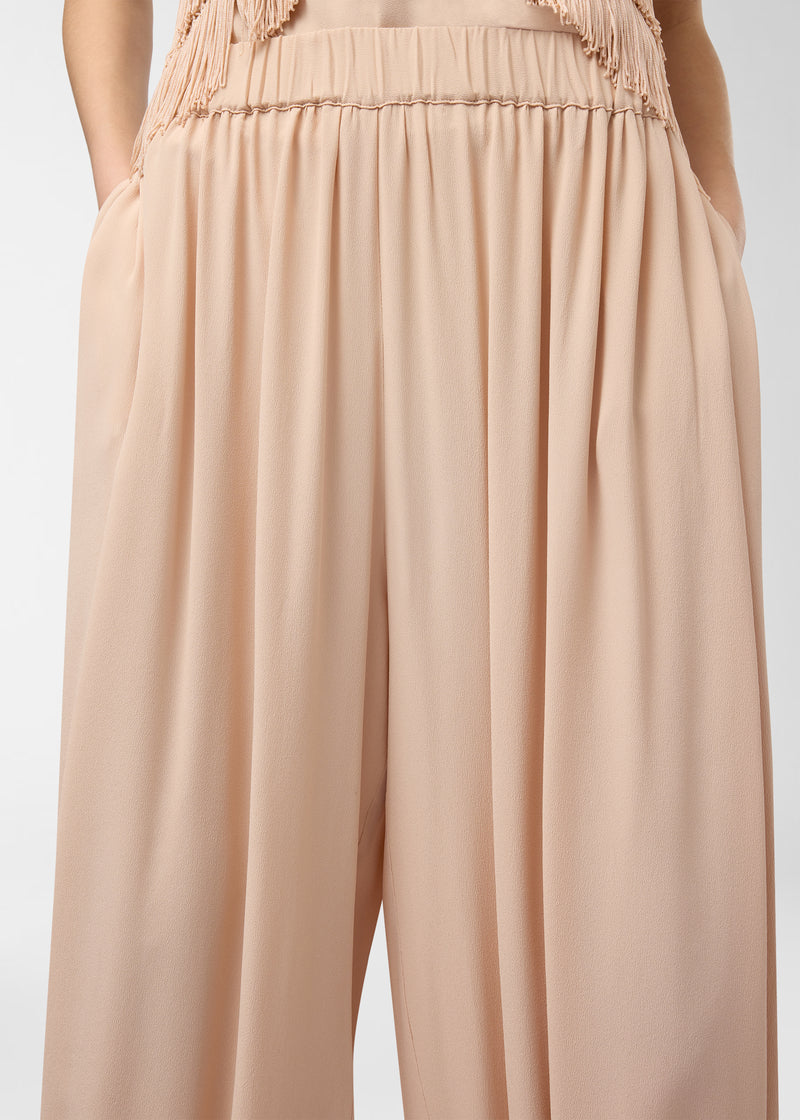 Frontal view — Noor Maxi Pants: peach crepe de chine drapes in wide, balloon-shaped legs; gathered low-rise elastic waistband with bow; tapered ankles and hands in side pockets.